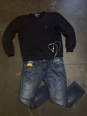 Mörkblå stickad tröja från Polo Ralph Lauren - Klassisk mörkblå stickad tröja från Polo Ralph Lauren med rund halsringning och röd broderad logga på bröstet. Tröjan har långa ärmar och ribbade muddar vid ärmslut och nederkant. Perfekt till lager på lager och enkel att matcha.