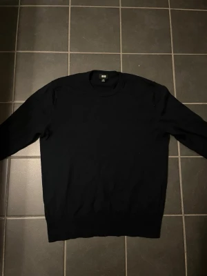 Merino ull tröja från Uniqlo - En stilren svart stickad tröja från Uniqlo med rund halsringning och långa ärmar. Tröjan har en klassisk passform och ribbade muddar vid ärmslut och nederkant. Perfekt basplagg för garderoben. Storleken är XS