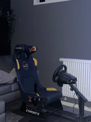 Playseat Red Bull Racing Esports stol - Säljer en Playseat Red Bull Racing Esports gamingstol  Stolen är mörkblå med gula detaljer och Red Bull-logga, tillverkad i tyg och metall. Perfekt för racing- och simulatorupplevelser hemma.