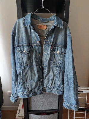 Klassisk blå jeansjacka från Levi's - Snygg blå jeansjacka från Levi's med klassisk passform, två bröstfickor med knappar och sidofickor. Jackan har silverfärgade knappar och ikonisk röd Levi's-tagg på bröstfickan. Tillverkad i slitstarkt denimtyg, perfekt för en avslappnad streetstil.