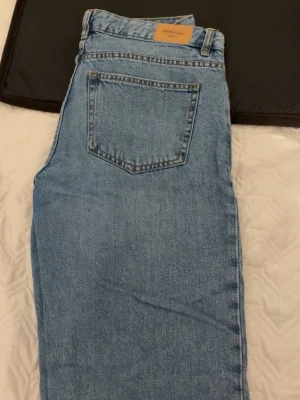 Blå mom jeans från Gina Tricot - Säljer ett par klassiska blå mom jeans från Gina Tricot. Jeansen har hög midja, raka ben och fem fickor. Tillverkade i mjuk denim med en ljus tvätt och bälteshällor. Perfekta för en avslappnad och trendig look.