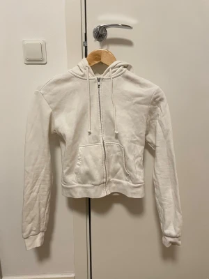 Vit croppad zip-kofta  - Snygg och basic hoodie-kofta med dragkedja framtill och luva. Perfekt till allt yäni – jeans, mjukis eller kjol.  Storlek: XS men sitter som en mindre modell. Passform: croppad modell, sitter tajt och kort i midjan  Skick: bra skick, inga större defekter