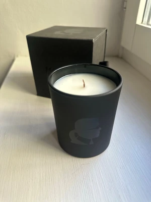 Doftljus från Karl Lagerfeld  - Snyggt doftljus från Karl Lagerfeld i svart glasbehållare med ikoniskt tryck av Karl Lagerfelds profil. Kommer i matchande svart kartong. Perfekt som inredningsdetalj för dig som gillar stilrena accessoarer och design.