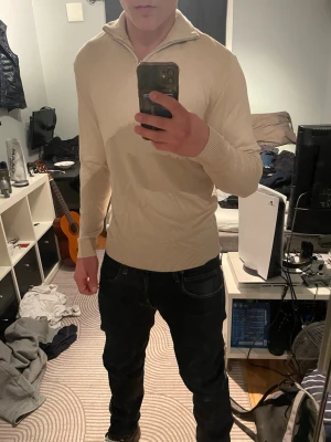 Beige stickad tröja med halv dragkedja - Snygg beige stickad tröja från Vila med halv dragkedja i halsen och ribbade muddar. Tröjan har en hög krage som kan vikas ner och är tillverkad i mjukt material. Perfekt för dig som gillar stilrena och enkla plagg.