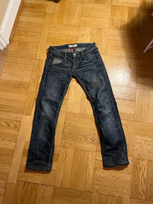 Mörkblå jeans från G-Star RAW - Säljer ett par mörkblå jeans från G-Star RAW med snygga slitningar och kontrastsömmar. Jeansen har raka ben, fem fickor och detaljer i grått vid fickorna. Klassisk knappgylf och läderpatch bak i midjan.