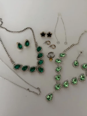 Set med gröna och silverfärgade smycken - Säljer ett mixat smyckeset med halsband, armband och örhängen i silverfärg med gröna och klara stenar. Inkluderar droppformade örhängen och halsband med gnistrande stenar, samt svarta och guldiga örhängen. Perfekt för dig som gillar statement-smycken.