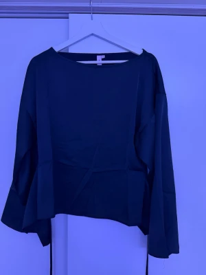 Svart blus med knytband bak från Nelly 💗 - Stilren svart blus med vida och långa ärmar, och rund halsringning. Blusen har ett snyggt knytband i ryggen som ger en unik detalj. Tillverkad i ett mjukt, lätt tyg som faller fint. Toppen är i storlek 34 och är oanvänd. Kan skicka fler och bättre bilder om det önskas 💗😇