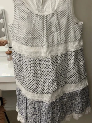 Vit och blå prickig kortklänning - Söt kortklänning i vitt och blått med prickigt mönster och spetsdetaljer. Klänningen är ärmlös och har flera lager med volang längst ner. Perfekt för sommarens varma dagar.