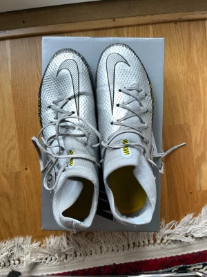 Nike phantom skorpion edition  - Snygga vita phantom  fotbollsskor från Nike med skorpion editionr och gula inslag. Skorna har snörning, stickad ovandel och robusta dobbar för bra grepp på planen. Perfekta för dig som vill ha stilrena och funktionella skor till match eller träning. Finns bara några i världen