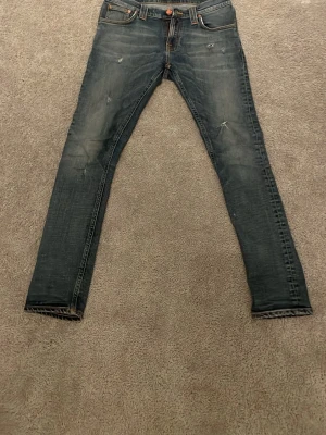 Nudie jeans - Säljer ett par blå jeans från nudie med snygga slitningar och tvättade detaljer. Jeansen är i mycket bre skick. Storlek 28 30