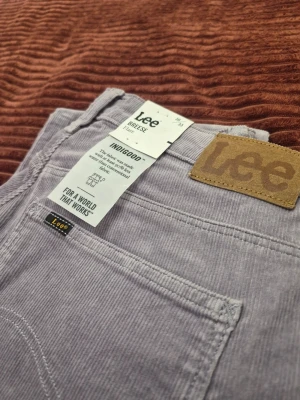Helt nya! Vintage Lee Breese Flare high-waist corduroy lila byxor, storlek 30 33 - Snygga ljuslila manchesterbyxor från Lee med klassisk femficksdesign och raka ben. Byxorna har ett Lee-läderpatch bak och är tillverkade i mjukt manchestertyg som ger en cool retrovibe. Perfekta för dig som vill sticka ut med färg och stil.