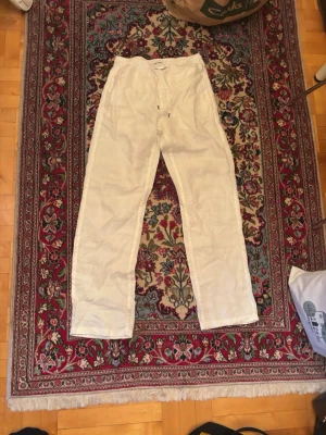 Vita linnebyxor från Brothers - Snygga vita linnebyxor med avslappnad passform och dragsko i midjan. Perfekta för en chill och stilren look. Byxorna är raka i modellen och har en klassisk design som funkar till många outfits. Nypris: 1400kr
