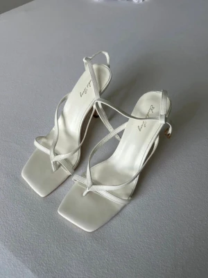Vita pumps med remmar från Amazon. - Stilrena vita pumps med smala, korsade remmar och fyrkantig tå från Las Attias(Amazon). Skorna har medelhög klack och justerbar ankelrem. Materialet är slätt konstläder som ger en elegant och modern vibe.