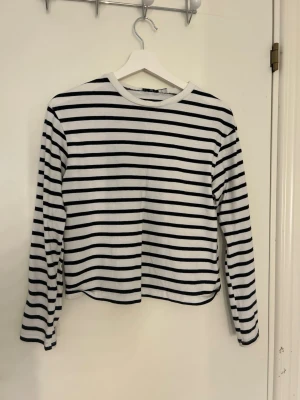 Randig långärmad topp  - Säljer en vit och svart långärmad topp med klassiska horisontella ränder. Toppen har en rak passform och rund halsringning. Perfekt att styla med jeans eller kjol för en enkel och snygg look.