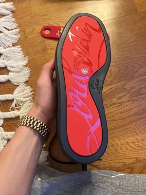 Christian Louboutin svarta sneakers - Säljer ett par svarta sneakers från Christian Louboutin med den ikoniska röda sulan och diskret logga på sidan. Skorna är i mocka och har svarta snören samt svarta detaljer. Perfekta för dig som vill sticka ut med en lyxig och stilren look.
