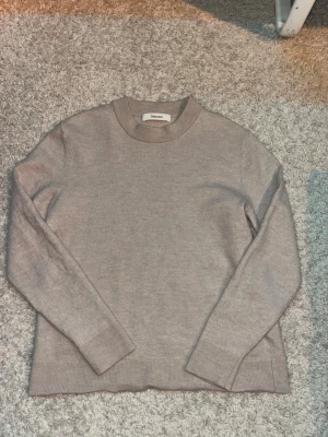 Beige stickad tröja från Selected - En stilren beige stickad tröja från Selected med rund halsringning och långa ärmar. Tröjan har ribbade muddar vid ärmslut och nederkant, vilket ger en klassisk och clean look. Perfekt att matcha med jeans eller kjol.