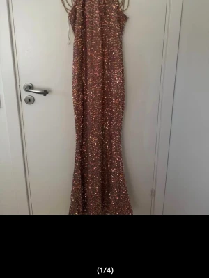 Lång paljettklänning i rosa/guld - Säljer en lång, glittrig klänning täckt med guldiga paljetter. Klänningen har smala axelband och en figurnära passform som ger en elegant siluett. Perfekt för dig som vill sticka ut på bal eller fest! Materialet är syntet med paljettdetaljer.