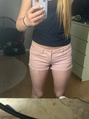 Ljusrosa shorts från ONLY - Säljer ett par ljusrosa shorts från ONLY med råa kanter och klassisk femficksdesign. Shortsen har låg midja och är perfekta för varma dagar. Stängs med knapp och dragkedja framtill. Passar storlek XS/S