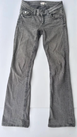 Grå bootcut jeans - Säljer ett par gråa bootcut jeans med klassisk femficksdesign. Jeansen har en rak passform upptill och lätt utsvängda ben. Tillverkade i ett mjukt denimtyg som ger en avslappnad look. 