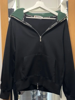 Svart hoodie från BAPE - Säljer en svart hoodie från BAPE med dragkedja hela vägen och stor ficka framtill. Huvan har grön camo-mönstrad insida och coola detaljer. Använd endast ett fåtal gånger. Passar M/S