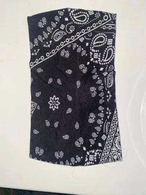 Svart bandana hårband paisleymönster - Snyggt svart hårband med klassiskt vitt paisleymönster i bandanastil. Tillverkat i mjukt tyg med twistad detalj framtill som ger en trendig look. Perfekt accessoar för att lyfta din frisyr och hålla håret på plats.