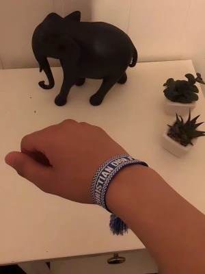 Dior armband - Snyggt blått tygarmband från Christian Dior med vit text och dekorativa tofsar i ändarna. Armbandet har ett vävt mönster och justerbar knytning för perfekt passform. Perfekt accessoar för att lyfta din outfit med en exklusiv touch.