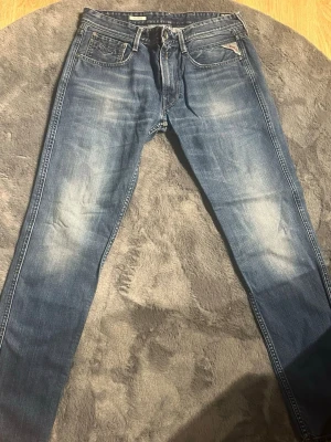 Blå Replay jeans med slitningar - Snygga blå jeans från Replay med klassisk femficksmodell och tydliga slitningar på låren och knäna. Jeansen har raka ben och detaljerad söm vid fickorna samt Replay-logga på myntfickan. Tillverkade i denim med en cool tvättad look.