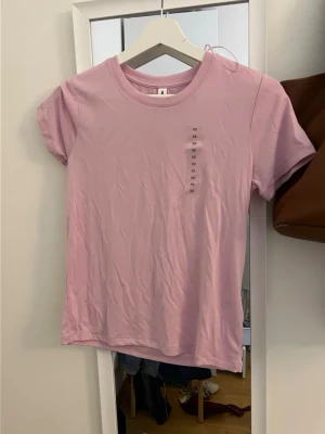Ljusrosa t-shirt från Ader Error - Säljer en ljusrosa t-shirt från Ader Error med rund hals och korta ärmar. Tillverkad i träningsmaterial, helt oanvänd!