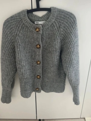 Grå stickad kofta från ZARA - Mysig grå stickad kofta från ZARA med grov ribbstickning och stora bruna knappar framtill. 