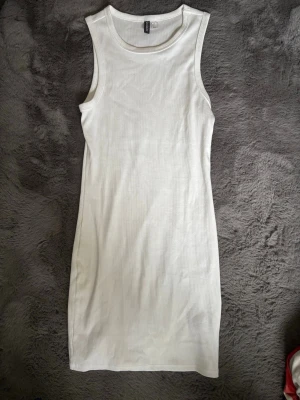 Vit ribbad ärmlös klänning H&M Divided - Säljer en enkel och stilren vit ribbad klänning från H&M Divided. Klänningen är ärmlös, har rund halsringning och är i kort modell. Perfekt att styla med sneakers eller sandaler för en avslappnad look.