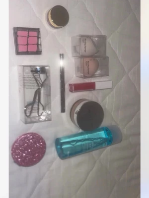 Makeupverktyg och tillbehör kit - Säljer ett kit med sminkverktyg och tillbehör: rosa ögonskuggspalett, två makeupsvampar i förpackning, ögonfransböjare, svart eyelinerpenna, rosa läppglans, puder, blå sminkborttagning, och en rosa glittrig spegel. Perfekt för dig som vill ha allt samlat! 100kr för allt(bara läppglanset kostar 150 nytt) 