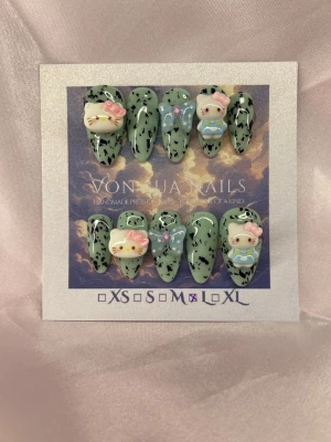 MintKitty (L);Medium Almond - Unika handgjorda press-on naglar i grönt med svart mönster och söta 3D dekorationer; Hello Kitty. Naglarna har en medium lång almond form och dekoreras med pastellfärgade rosetter och detaljer. Perfekt för dig som vill ha något gulligt och trendigt på naglarna.L: 17 mm, 12,5 mm, 13 mm, 12 mm, 10 mm 