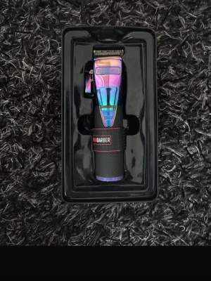 BabylissPRO hårtrimmer regnbågsfärgad - Säljer en BabylissPRO hårtrimmer i regnbågsfärgad metallic med svart grepp och röda detaljer. Medföljer flera svarta plastkammar i olika storlekar för flexibel styling. Perfekt för dig som vill ha en snygg och unik trimmer till håret.