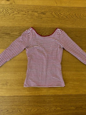 Rödvit randig långärmad topp H&M - Säljer en långärmad topp från H&M i rödvitt randigt mönster. Toppen har en rundad halsringning och är figurnära i modellen. Perfekt att styla med jeans eller kjol för en enkel och snygg look.