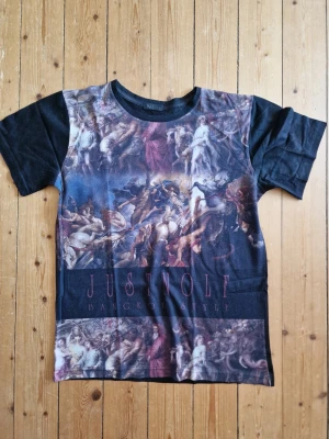 Unik t-shirt med konstmotiv Medium fint skick  - Fint skick, knappt använd. Står Large men är mer som en Medium. Unik svart t-shirt från Nolf med ett stort konstmotiv över hela framsidan. Trycket föreställer en klassisk målning med dramatiska figurer och färger. T-shirten har rund hals och korta ärmar, perfekt för dig som vill sticka ut.