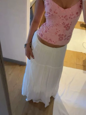 Vit långkjol med volangdetaljer - Säljer en flowy vit långkjol med flera volanglager och en avslappnad passform. Kjolen har en mjuk struktur och är perfekt för varma dagar. Styla med ett bälte för extra detalj eller bär den som den är för en enkel look.
