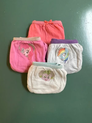 My Little Pony trosor 4-pack - Fyra par färgglada trosor med My Little Pony-motiv. Färgerna är rosa, ljusrosa, grå och vit med kontrasterande muddar. Motiven inkluderar Pinkie Pie, Rainbow Dash och Spike. Tillverkade i mjuk bomull för skön känsla hela dagen.