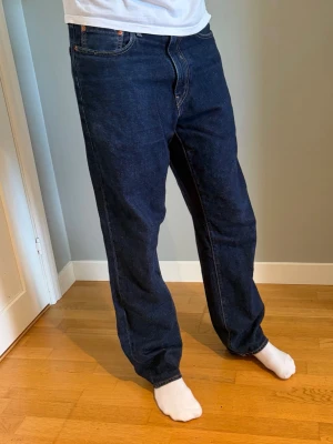 Levi’s straight fit - Säljer ett par mörkblå jeans med rak passform och klassisk femficksdesign. Jeansen har orange sömmar och är tillverkade i denim. Perfekta för dig som gillar en enkel och tidlös stil. Är 185 och sitter bra
