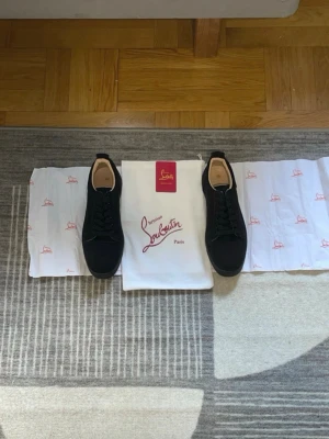 Svarta sneakers från Christian Louboutin - Stilrena svarta sneakers från Christian Louboutin med klassisk låg profil och svarta skosnören. Skorna har en diskret design och är tillverkade i mocka med detaljer i läder. Perfekta för dig som gillar exklusiva och tidlösa sneakers.