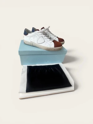 Philippe Model vita och bruna sneakers - Snygga vita sneakers från Philippe Model med bruna detaljer på tån och hälen samt blå inslag baktill. Skorna har en klassisk låg siluett, vita skosnören och en beige sula. Tillverkade i läder och mocka för en exklusiv känsla.