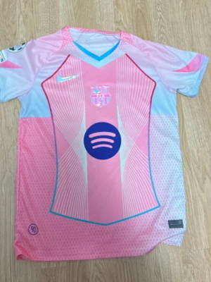 Barça rosa matchtröja Lamine Yamal - Snygg rosa och ljusblå FC Barcelona matchtröja från Nike med Lamine Yamal och nummer 10 på ryggen. Tröjan har klubbmärke, Nike-logga och Spotify-logga på bröstet samt Champions League-märke på ärmen. Perfekt för fotbollsfans!