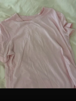 Ljusrosa basic t-shirt - En enkel och stilren ljusrosa t-shirt i mjuk bomull. T-shirten har rund halsringning och korta ärmar, perfekt för en avslappnad look. Passformen är normal och tyget känns skönt mot huden.