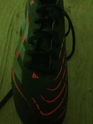 Svarta fotbollsskor med röda detaljer - Säljer ett par svarta fotbollsskor med röda och gråa detaljer samt snörning. Skorna har en modern design med mönstrade linjer på ovandelen och klassiska ränder på sidan. Perfekta för dig som vill sticka ut på planen. Men dom är club 