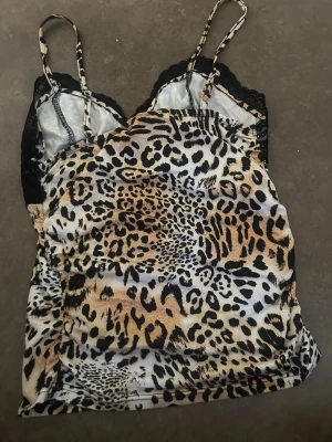 Leopardmönstrad body med spetsdetaljer - Snygg body med leopardmönster i beige, svart och brunt. Justerbara smala axelband och svarta spetsdetaljer vid bysten ger en extra touch. Perfekt för dig som gillar djurmönstrat och vill ha något unikt i garderoben.