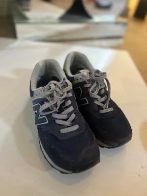 Marinblå New Balance sneakers - Snygga marinblå sneakers från New Balance med grå detaljer och vita skosnören. Skorna har en klassisk låg siluett, meshpartier för andningsförmåga och mockaliknande material på ovandelen. Perfekta för en sportig och avslappnad stil.