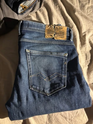 Blå slim fit jeans Replay - Snygga blå slim fit jeans från Replay med klassisk femficksdesign och slitna detaljer på bakfickan. Jeansen har en något tvättad look och är tillverkade i ett mjukt denimtyg som sitter skönt. Perfekta för dig som gillar en smalare passform.