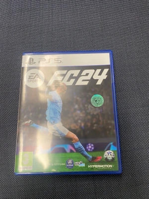 EA Sports FC24 till PS5 - Säljer spelet EA Sports FC24 till PlayStation 5. Spelet kommer i ett blått plastfodral med omslagsbild på en fotbollsspelare i ljusblå matchställ. Inuti finns spelmanual och skiva med svart design och vit text. Perfekt för dig som gillar fotbollsspel!
