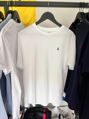 Vit t-shirt från Polo Ralph Lauren - Klassisk vit t-shirt från Polo Ralph Lauren med den ikoniska lilla broderade loggan på bröstet. T-shirten har rund halsringning och korta ärmar. Tillverkad i mjuk bomull för en skön och avslappnad känsla.
