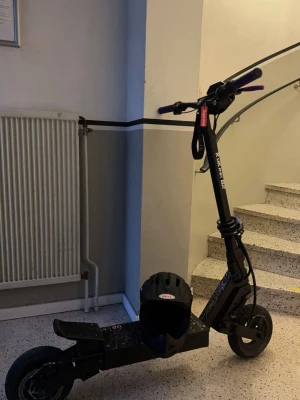 Svart elscooter kukirin g2 - Säljer en svart elscooter med robust ram och breda hjul. Styret har lila handtag och det följer med en svart hjälm från Bell. Scootern har en sportig design och passar perfekt för snabba turer i stan.