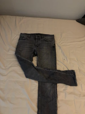 Mörkgrå Nudie Jeans Slim Fit - Säljer ett par mörkgrå slim fit jeans från Nudie Jeans. Klassisk femficksmodell med den ikoniska vågade sömmen på bakfickan. Jeansen har normal midja och är tillverkade i mjuk denim, perfekta för en avslappnad och stilren look.